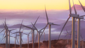 wind turbines, in the background mountaintops in fog coloured by the sunrise. It illustrates energy savings by TrumpJet® and Wetend's dedication to protect the environment 