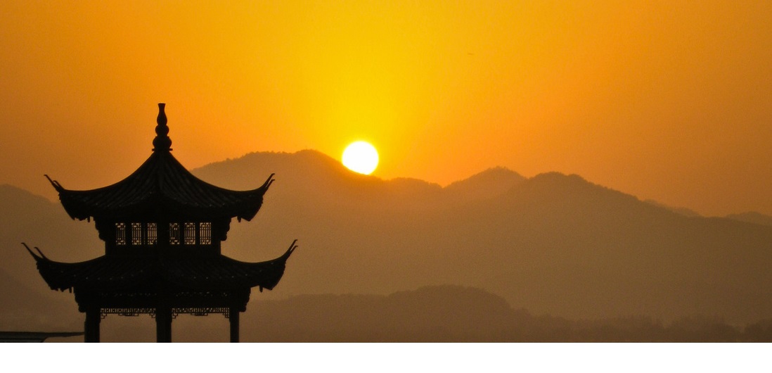 Sunrise over the mountain tops, at the front the silhouette of a Chinese pagoda